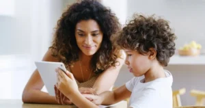 A mother looks at a tablet with her young child.